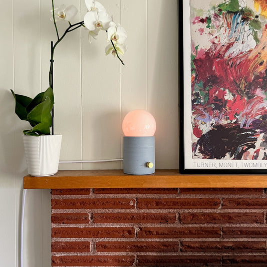 Decorative lamp on a wooden shelf with a plant and abstract art in the background.