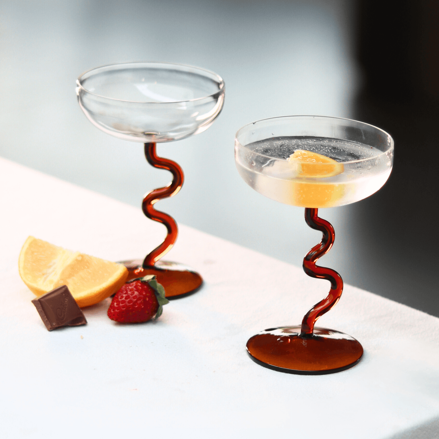 Amber Swirl Cocktail Glass Set with artisan design, showcasing handcrafted glasses beside lemon and strawberry.