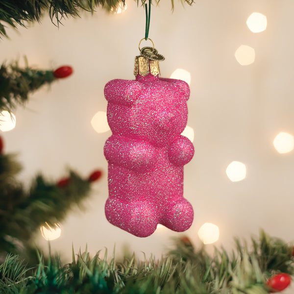 Pink glittery bear-shaped ornament on a Christmas tree with lights in the background