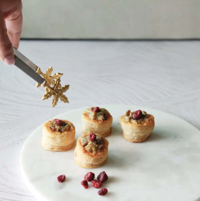 Hand holding Brass Leaf Tongs, elegantly serving delicious snacks on a marble platter. Perfect artisan decor!