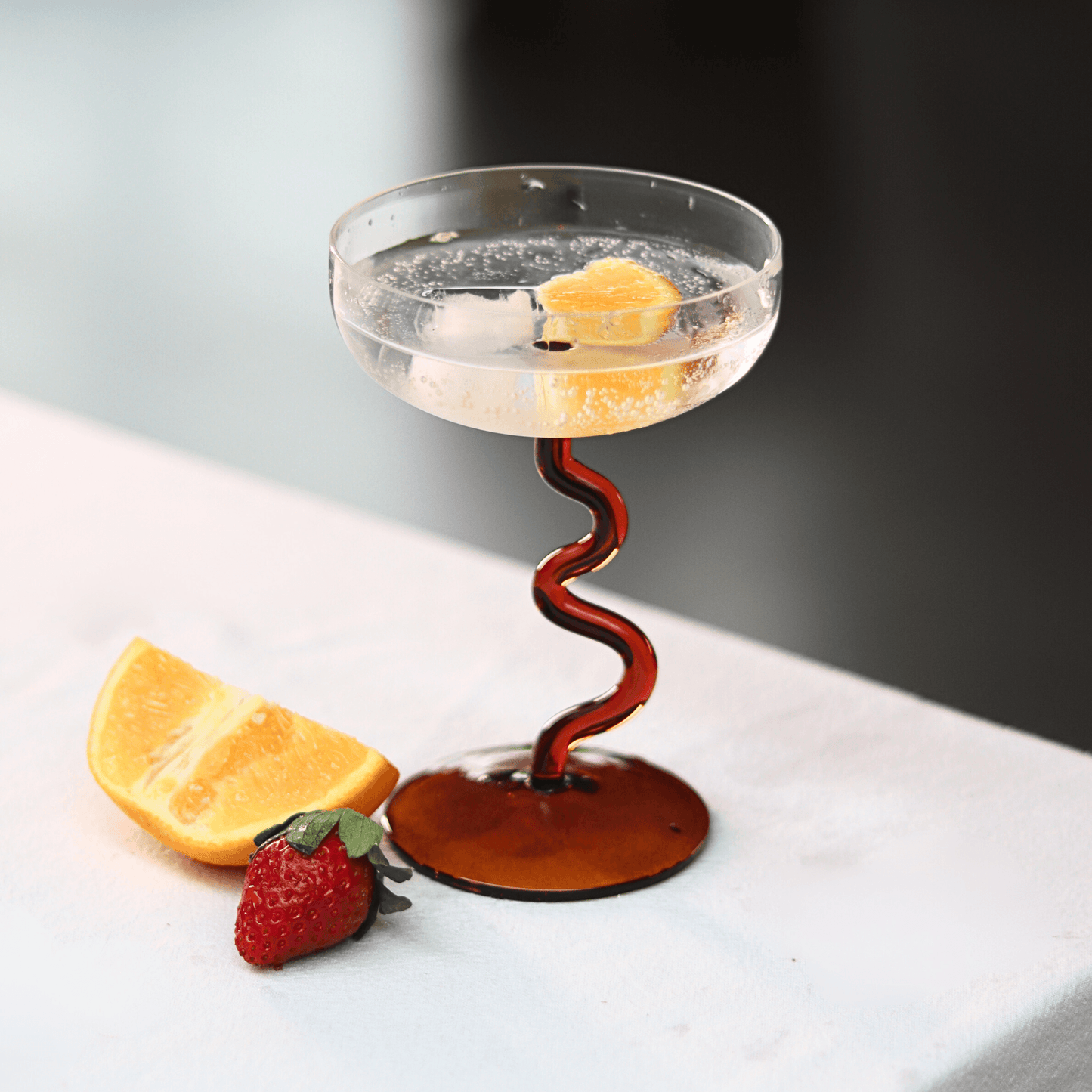 Amber Swirl Cocktail Glass Set filled with a sparkling drink, garnished with citrus and strawberry, showcasing artisan craftsmanship.
