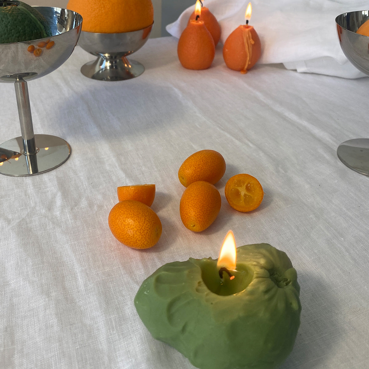 Cherimoya Candle glowing among vibrant kumquats and metallic decor, showcasing artisan handcrafted charm.